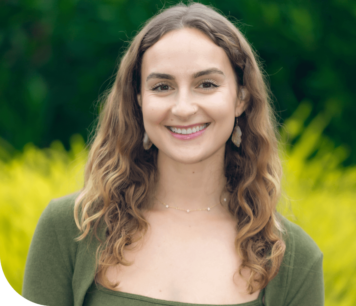 Smiling young woman with curly hair outdoors in a green setting.